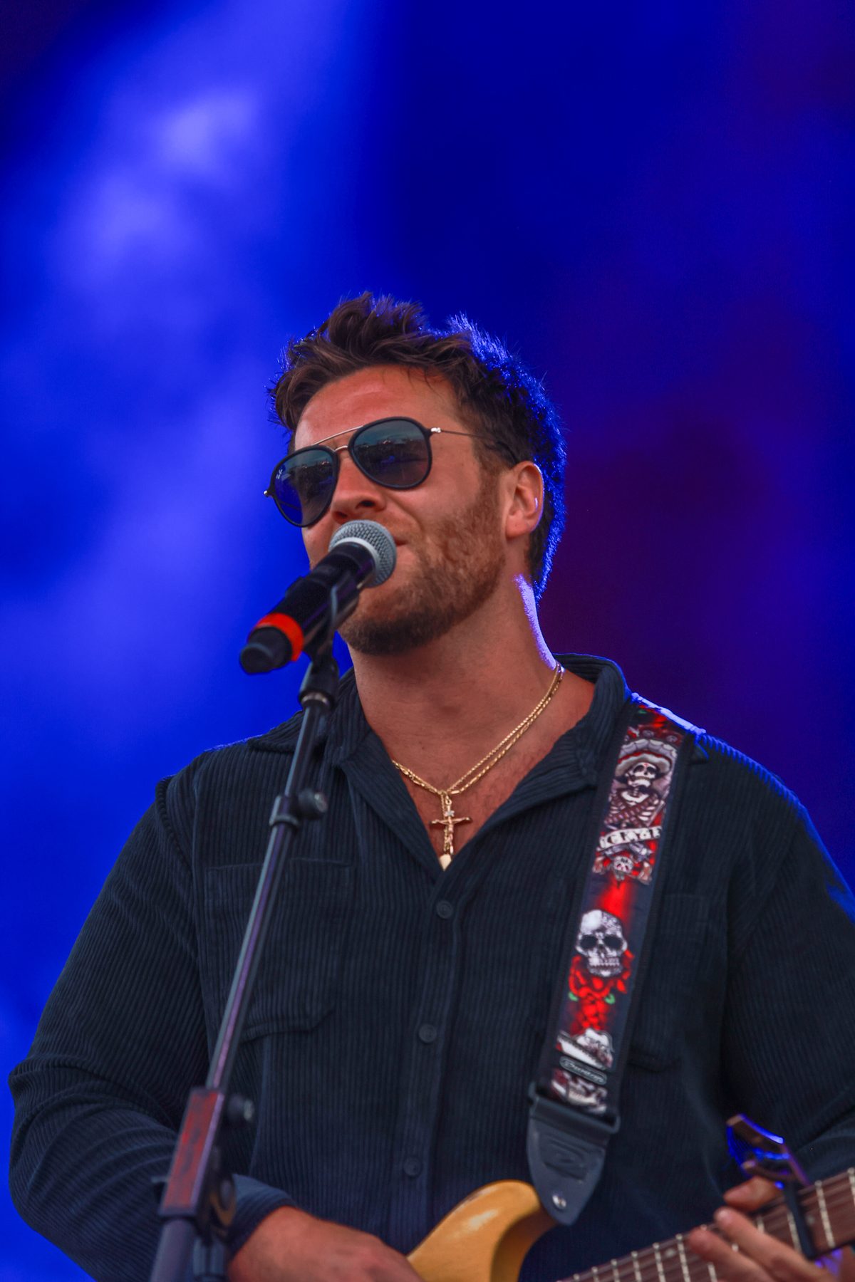 Brian Lawless singing into the microphone in blue stage light, guitar strap over his shoulder